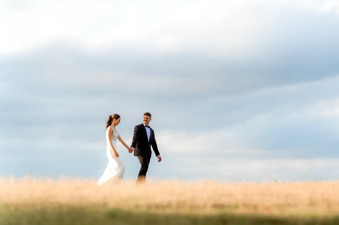 Bride and groom walking hand in hand through a golden field at Maroon Hill Estate