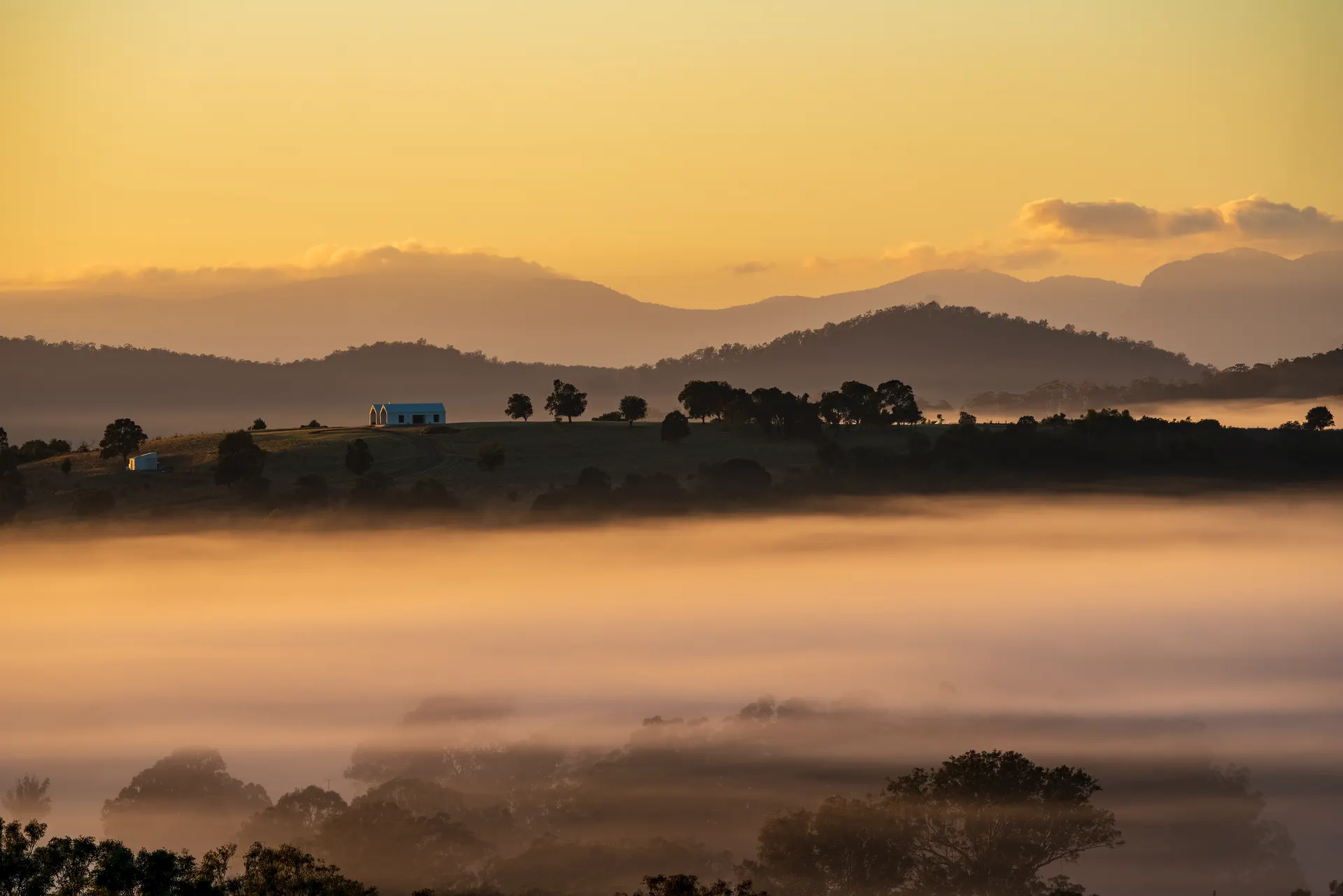 Maroon Hill Estate’s gabled venue on the hilltop above a sea of fog at sunrise, with mountains in the distance