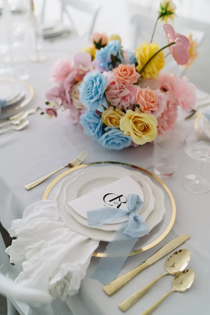 Table setting with a rainbow-hued floral centerpiece, gold cutlery and a monogrammed place card