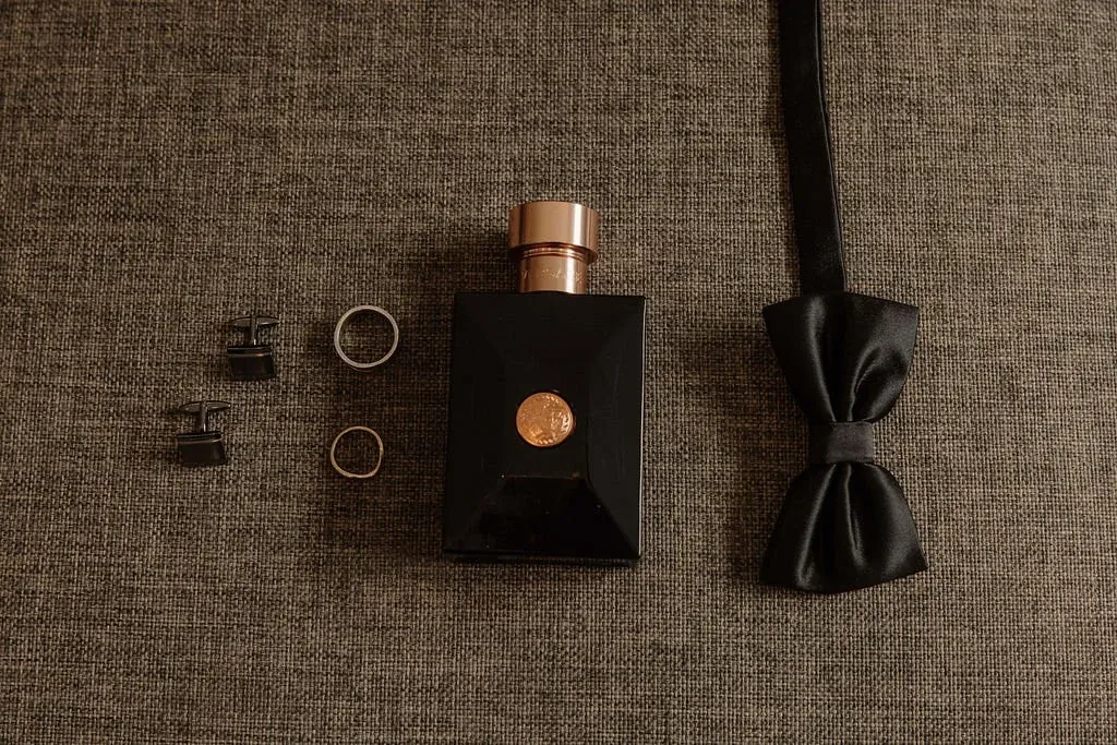 Groom's flat lay with cufflinks, wedding bands, cologne and a black bow tie