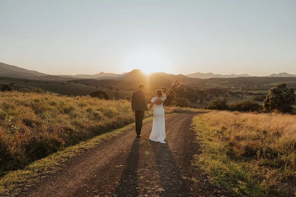 Nicola and Aaron walking hand in hand along a gravel road at sunset, mountain views at Maroon Hill Estate
