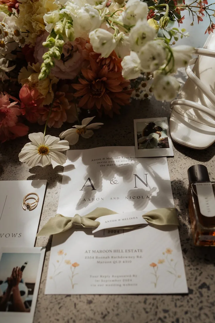 Wedding invitation suite with engagement rings, fresh florals and a polaroid photo styled on stone