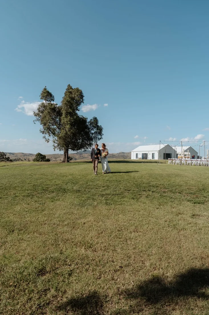 Nicola and Aaron walking across the lawn towards the reception barn at Maroon Hill Estate
