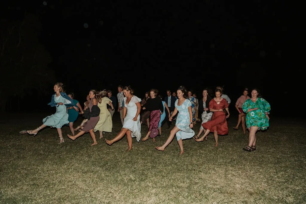 Guests dancing barefoot on the lawn under string lights at night