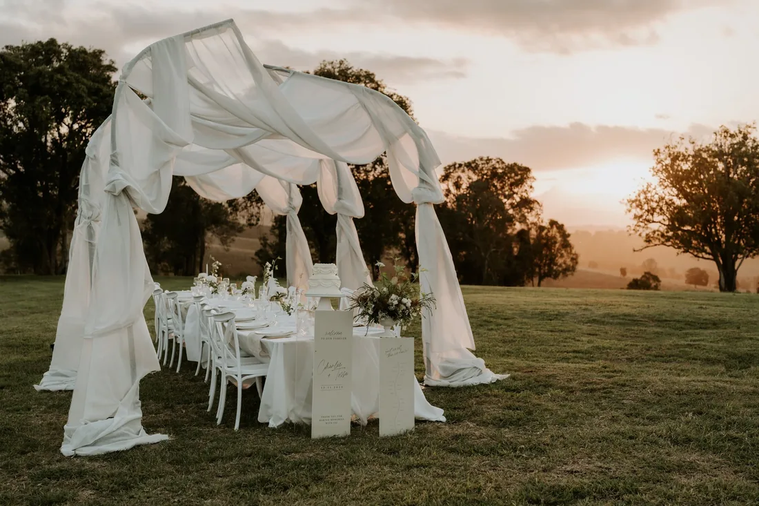 Sheer draped reception arbour styled over a long table on the lawn at golden hour