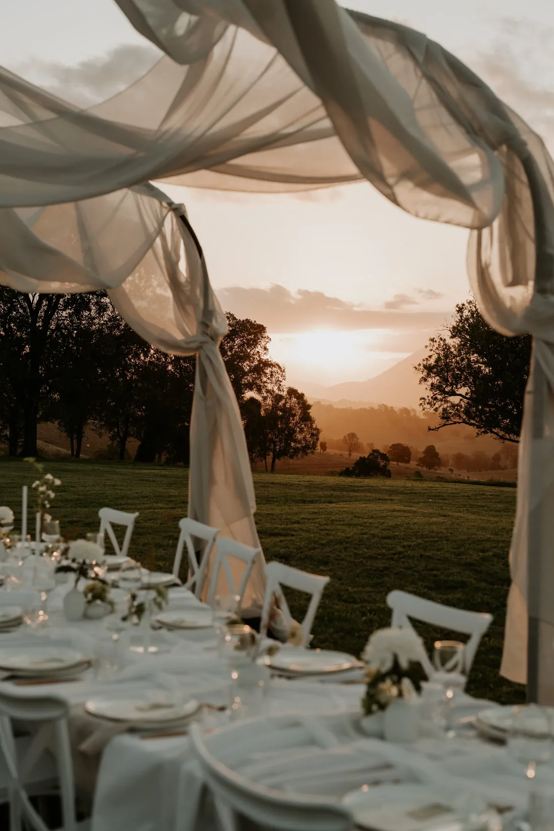 Sheer draped arbour framing a sunset table setting with the Scenic Rim mountains beyond