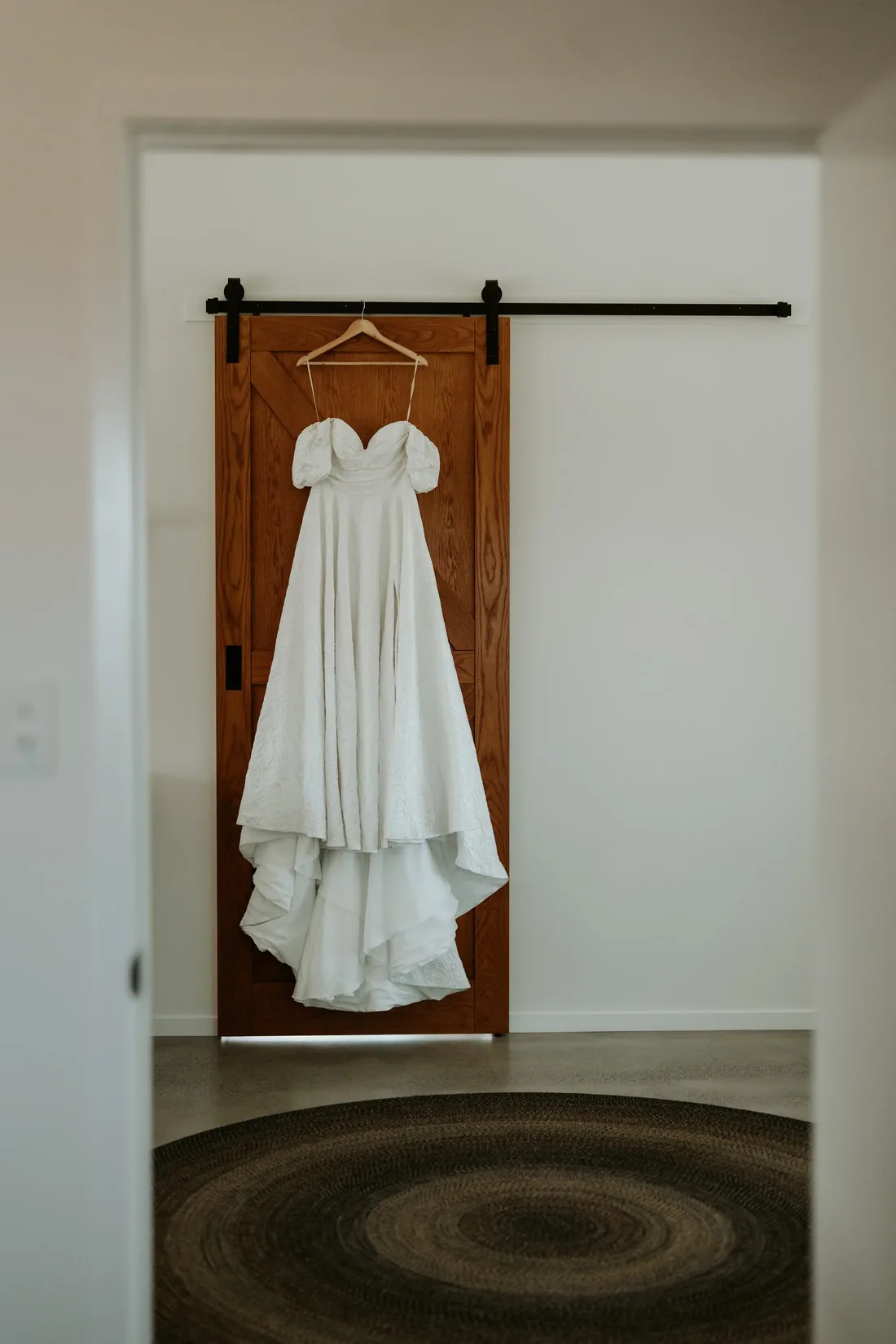 Wedding dress hanging on a rustic timber barn door, styled with a woven rug beneath