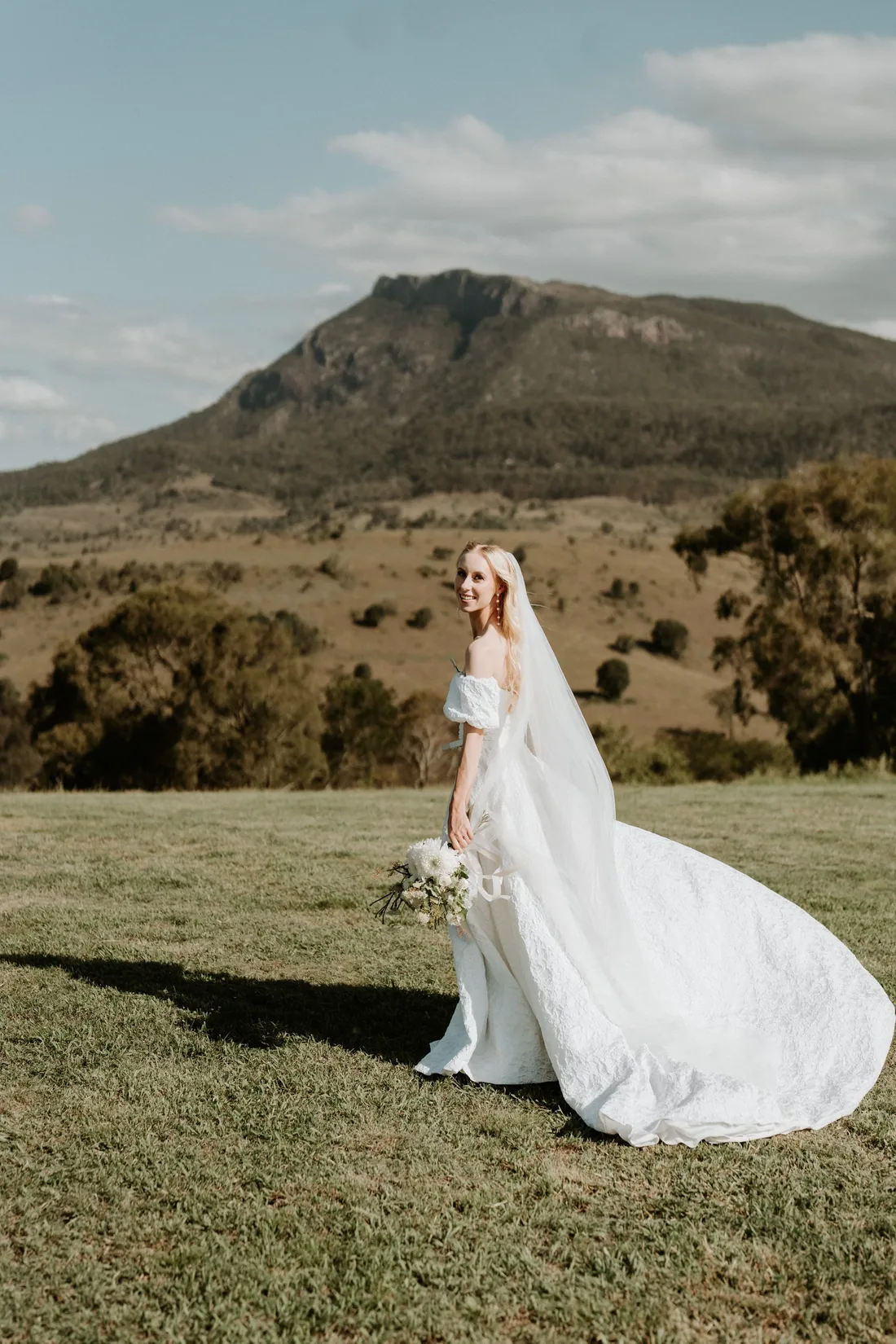 Bride walking through the grass with her cathedral veil trailing at Maroon Hill Estate