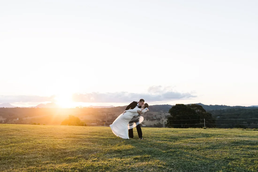 Sally and Joshua sharing a dip kiss at sunset in an open field at Maroon Hill Estate