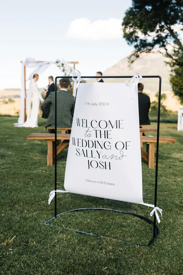 Welcome sign reading 'Welcome to the wedding of Sally and Josh' with the ceremony taking place behind it