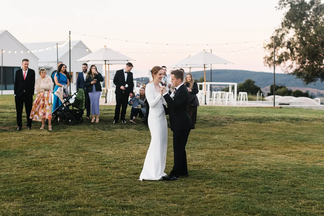 First dance on the lawn at dusk under festoon lighting, guests watching on