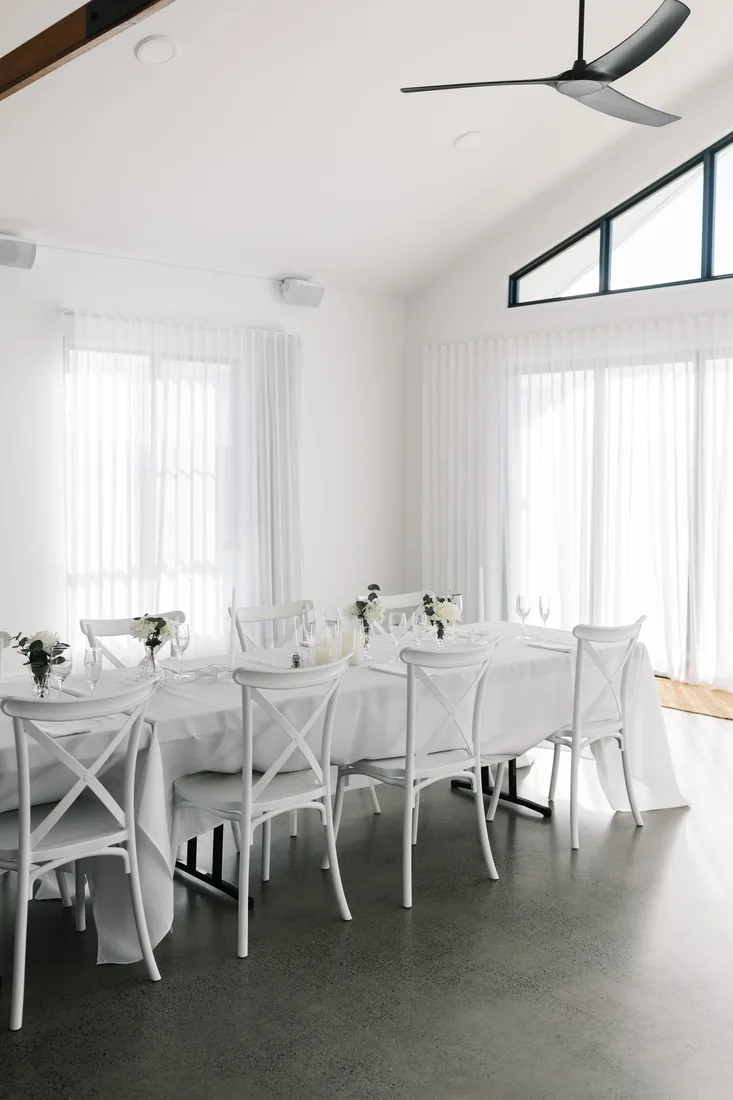 Reception table set indoors with white cross-back chairs, linen and florals at Maroon Hill Estate
