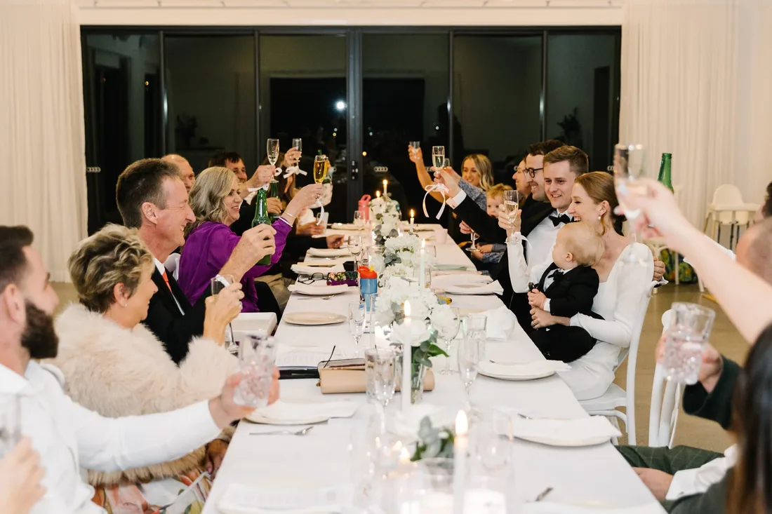 Guests raising champagne glasses in a toast at the reception table at night