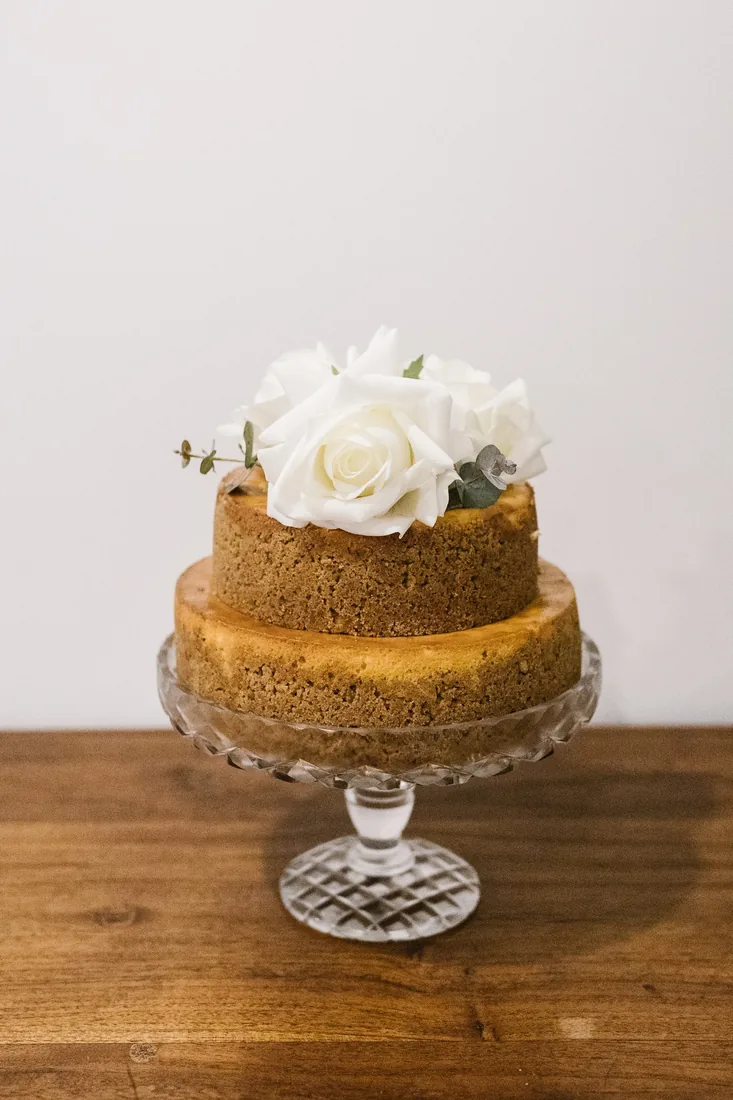 Two-tier naked wedding cake topped with a white rose on a glass cake stand